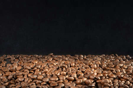one third of freshly roasted brown coffee beans with two thirds of black backgroundの写真素材