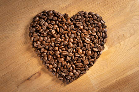 Brown freshly roasted coffee beans shaped into a love heart on oak wood backgroundの写真素材