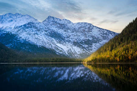 wonderfully calm lake Plansee with sun-lit green autumn forest and white snow-covered mountain in the backgroundの写真素材