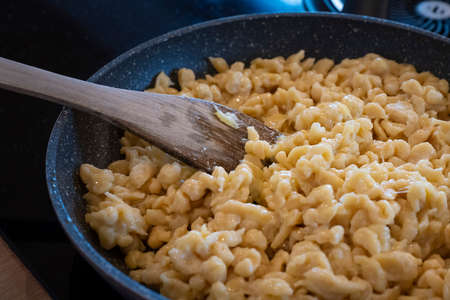 traditional tyrolean house dish kaesspatzn in a pan with a wooden spatula on the stovetopの写真素材
