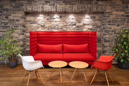 red modern couch chairs and tables illuminated with spotlights in front of retro natural stone masonryの写真素材