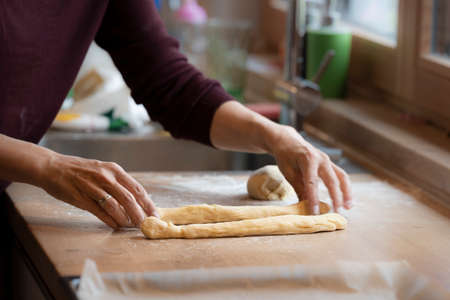 female hands roll and shape dough to bake an easter braidの写真素材
