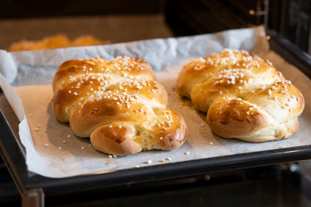 two freshly baked easter braids on a baking sheet in the oven with granulated sugar