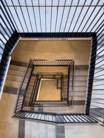 Bird's-eye view from top to bottom of stairwell in tall block of flats with banisters with black...