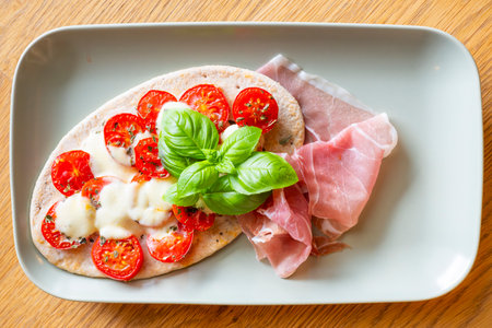 Tomato mozzarella pita on flatbread with fresh Parma ham and decorated with basil leaves served on a rectangular plateの写真素材