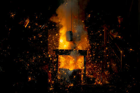 Foundry. Pouring hot metal from a ladle into molds. Bright red metal and sparks flying to the sidesの写真素材