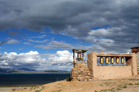 Small old Tibetan monastery and praying mills on a hill above holy Lake Manansovar, Tibetの写真素材