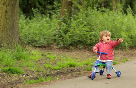 Little girl riding on her tricycle on a pathway in a park in springの写真素材