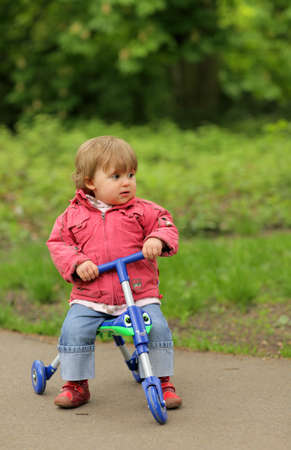 Little girl riding on her tricycle on a pathway in a park in springの写真素材