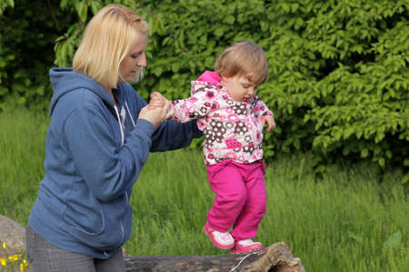 Mother safeguarding her daughter walking on a tree trunk in a park