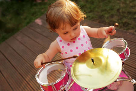Cute little girl playing toy drums in the home gardenの写真素材