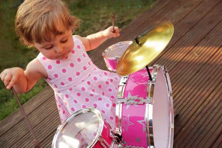 Cute little girl playing toy drums in the home gardenの写真素材