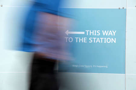 Blurred image of a person passing sign showing direction to the train stationの写真素材