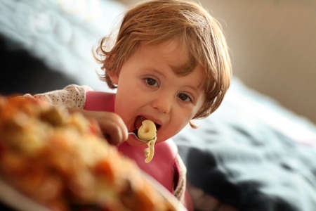 Portrait of a cute little baby girl eating pasta for dinnerの写真素材