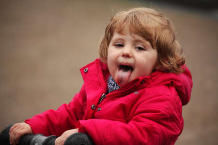 Little baby girl putting out a tongue while having fun in a playgroundの写真素材
