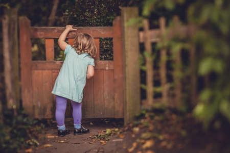 Young girl peeking through the hole in the small wooden gates in the gardenの写真素材