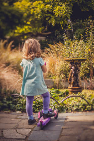 Little girl walking with her scooter on a pathway in a park in springの写真素材