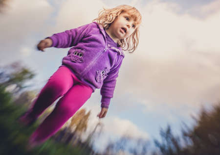 Cute little girl jumping high from the bench in a park in autumnの写真素材