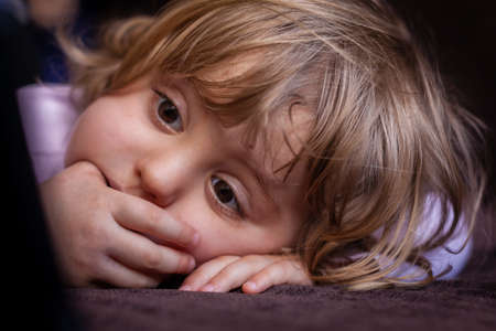 Little girl laying on a sofa and watching cartoon on a small tabletの写真素材