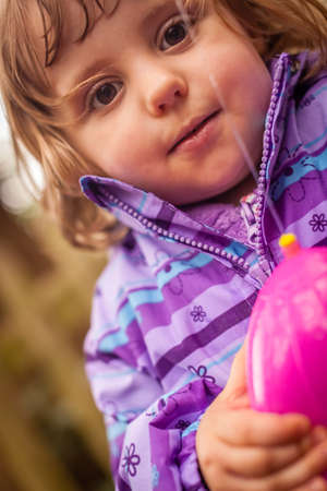 Little girl having fun spraying water with her plastic toy eggの写真素材