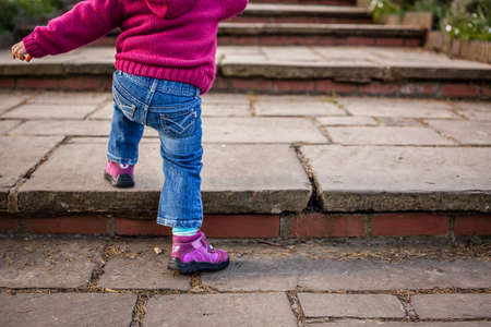 Cute baby girl climbing up the wide stairs in the parkの写真素材