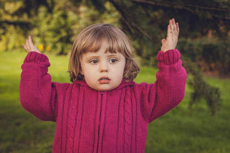 Little girl standing in the park with her hands up indicating her worriesの写真素材