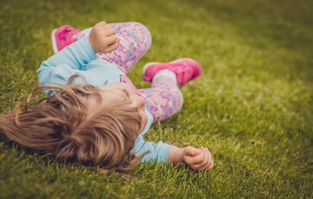 Little girl rolling downhill on the grass in a park in springの写真素材
