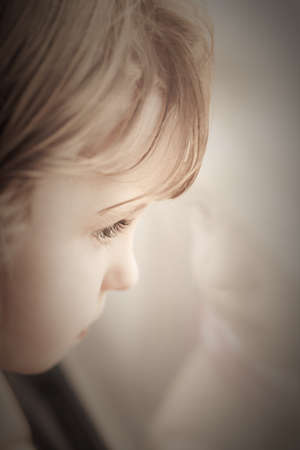 Portrait of a little baby girl looking through the windowの写真素材