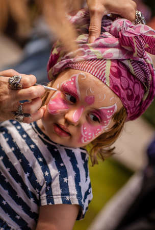 Little girl having her face painted during local fairの写真素材