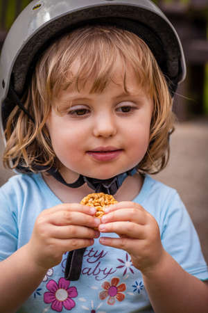 Little girl wearing small bike cycling helmet and eating biscuitの写真素材