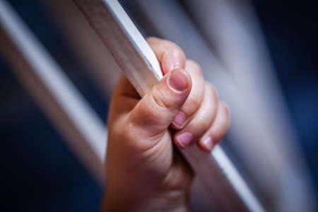 Baby hand holding to a metal railing of a fenceの写真素材