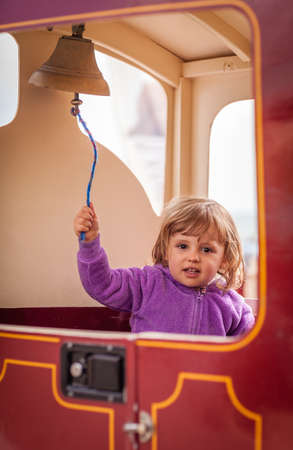 Little girl ringing a small bell in the toy train in an amusement parkの写真素材