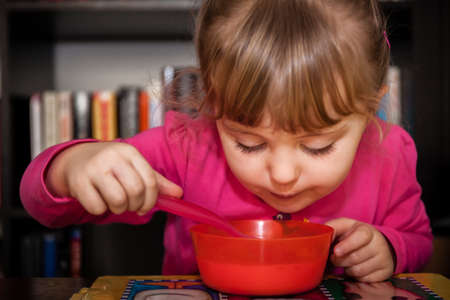 Portrait of a cute little baby girl eating milky porridge for breakfastの写真素材