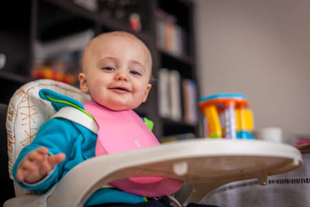 Little boy sitting in a high chair at home and waiting for a mealの写真素材