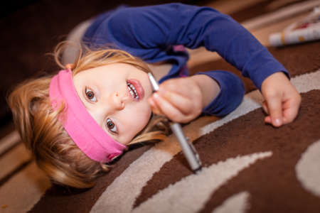 Little girl on the floor in her room holding pen, solving crosswordの写真素材