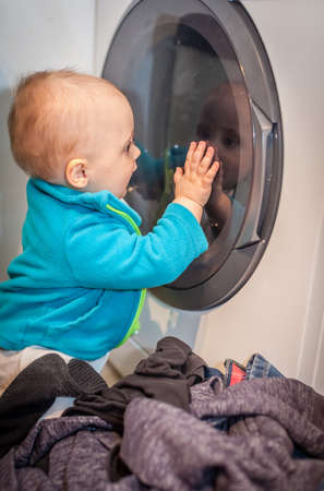 Portrait of a cute little baby boy looking with fascination inside the washing machineの写真素材