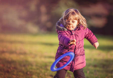 Little girl throwing flying disc in the park in autumnの写真素材