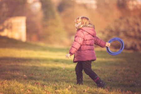Little girl throwing flying disc in the park in autumnの写真素材