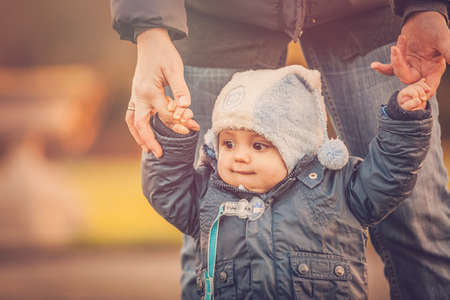 Little boy learning to walk with his mother in a park in early autumnの写真素材