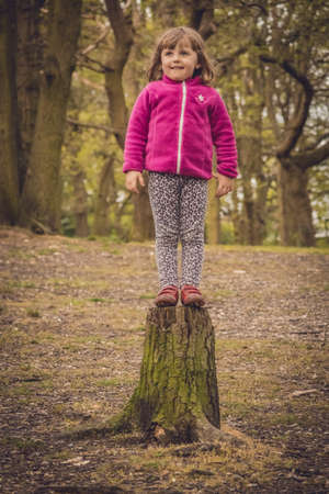 Little girl getting ready to jump from the cut tree in the forestの写真素材