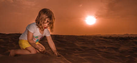 Little girl sitting on the sand on the sand dunes in  the Natural Reserve of Dunes of Maspalomas in Gran Canariaの写真素材