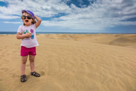 Little girl sitting on the sand on the sand dunes in  the Natural Reserve of Dunes of Maspaloma in Gran Canariaの写真素材