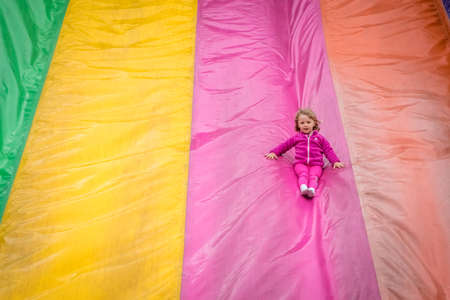 Little girl sliding down on a big inflatable mega slide in an outdoor funfair playgroundの写真素材