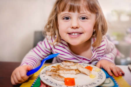 Portrait of a cute little baby girl eating chicken breast in breadcrumbs for lunchの写真素材