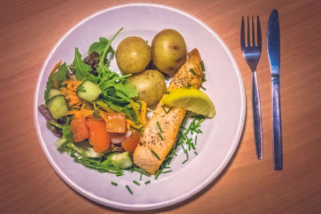 Roast salmon meal served with roasted baby potatoes and tomato, cucumber and carrot saladの写真素材