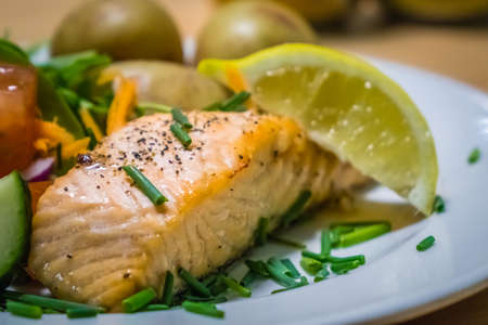 Roast salmon meal served with roasted baby potatoes and tomato, cucumber and carrot saladの写真素材