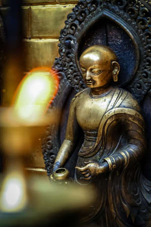 Brass figurine of a deity and candles burning inside one of the Buddhist temples in Nepalの写真素材
