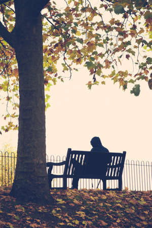 Man sitting alone on the bench on a cloudy, rainy autumn dayの写真素材