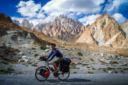 Solo male cyclist on the stunning road through Karakorum mountains in Pakistan, with Tupopdam peak in the background, Passu areaの写真素材