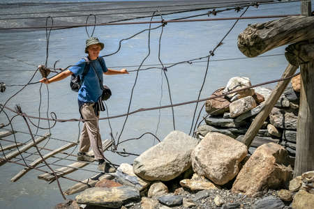 Woman traveller crossing the unstable bridge across Hunza river in Karakorumの写真素材